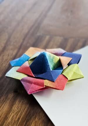 סביבון אוריגמי על גבי גלויית חג שמח עם סמל האנסו. סביבון ייחודי המקופל מניירות אוריגמי צבעוניים ויפהפיים , כל סביבון ייחודי ושונה. סביבון ממתוג, סביבון נייר, גלויית חג שמח, סדנאות סביבונים, סדנאות חנוכה, מתנות לחנוכה בעבודת יד. מורן אלחלל